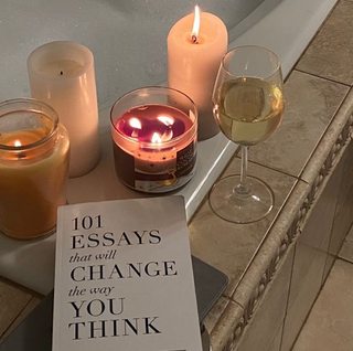 A candle, wine glass, and book on a bathroom counter.