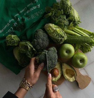 A person cutting vegetables with a green bag nearby.