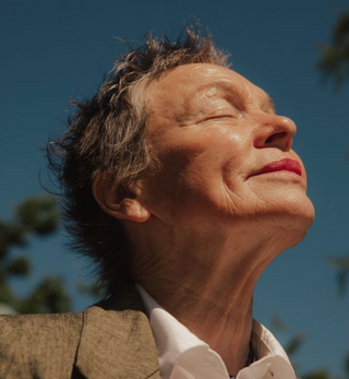 Elderly woman peacefully gazes at the sky with closed eyes.