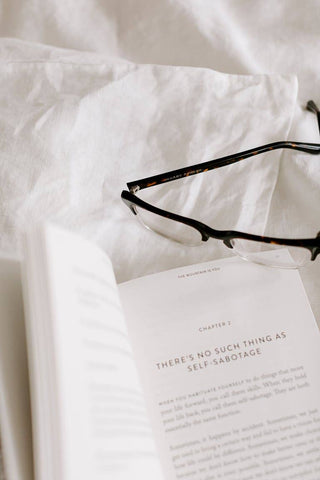 Glasses and book on bed, by Brianna Wiest