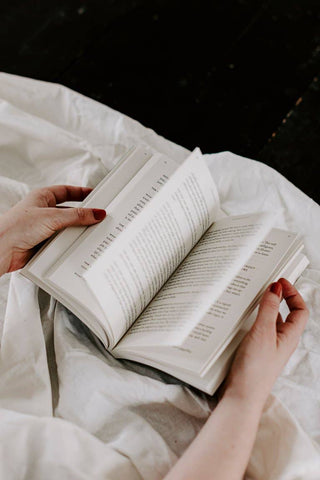 A woman peacefully reading a book while lying on a bed.
