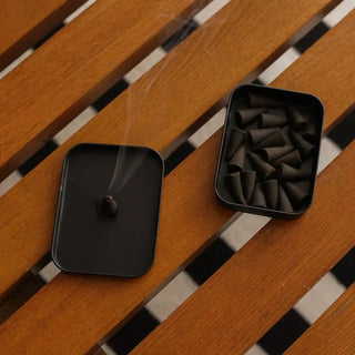 Black box with small candle on wooden bench.