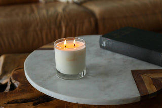 Lit candle beside a book on marble surface.