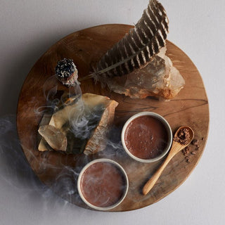 Wooden plate with two cups of hot chocolate and a feather on top.