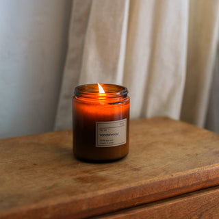 A candle on a wooden table, emitting a warm glow in a dimly lit room.