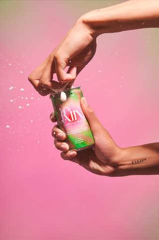 Hand holding soda can against pink backdrop.