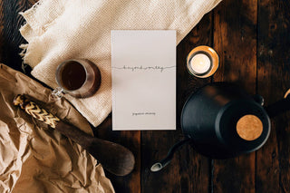 An arrangement of a book, tea pot, and candle on a table.