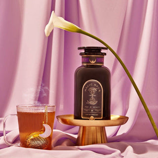 A bottle and cup of tea on a purple cloth.