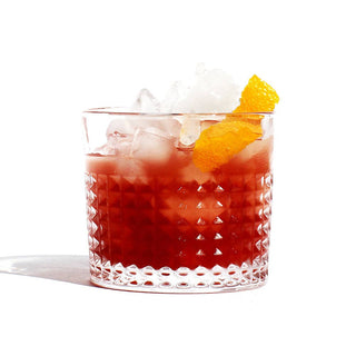 A glass of red drink with ice and orange peel, refreshing beverage perfect for a hot summer day.