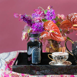 A tray with a floral tea pot, vibrant flowers, and a delicate vase, creating a charming and elegant arrangement.