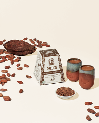 grain of cacao with a forward facing product box with two cups of freshly brewed cacao